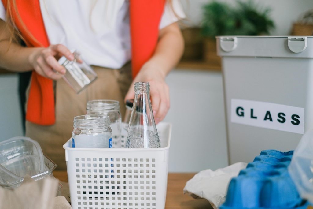 A woman sorts glass for recycling at home with bins, promoting eco-friendly practices.